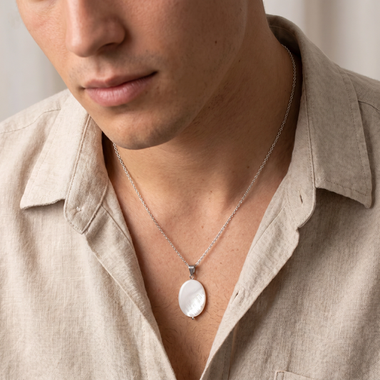 Man wearing a beige shirt with a silver necklace featuring a round pendant.