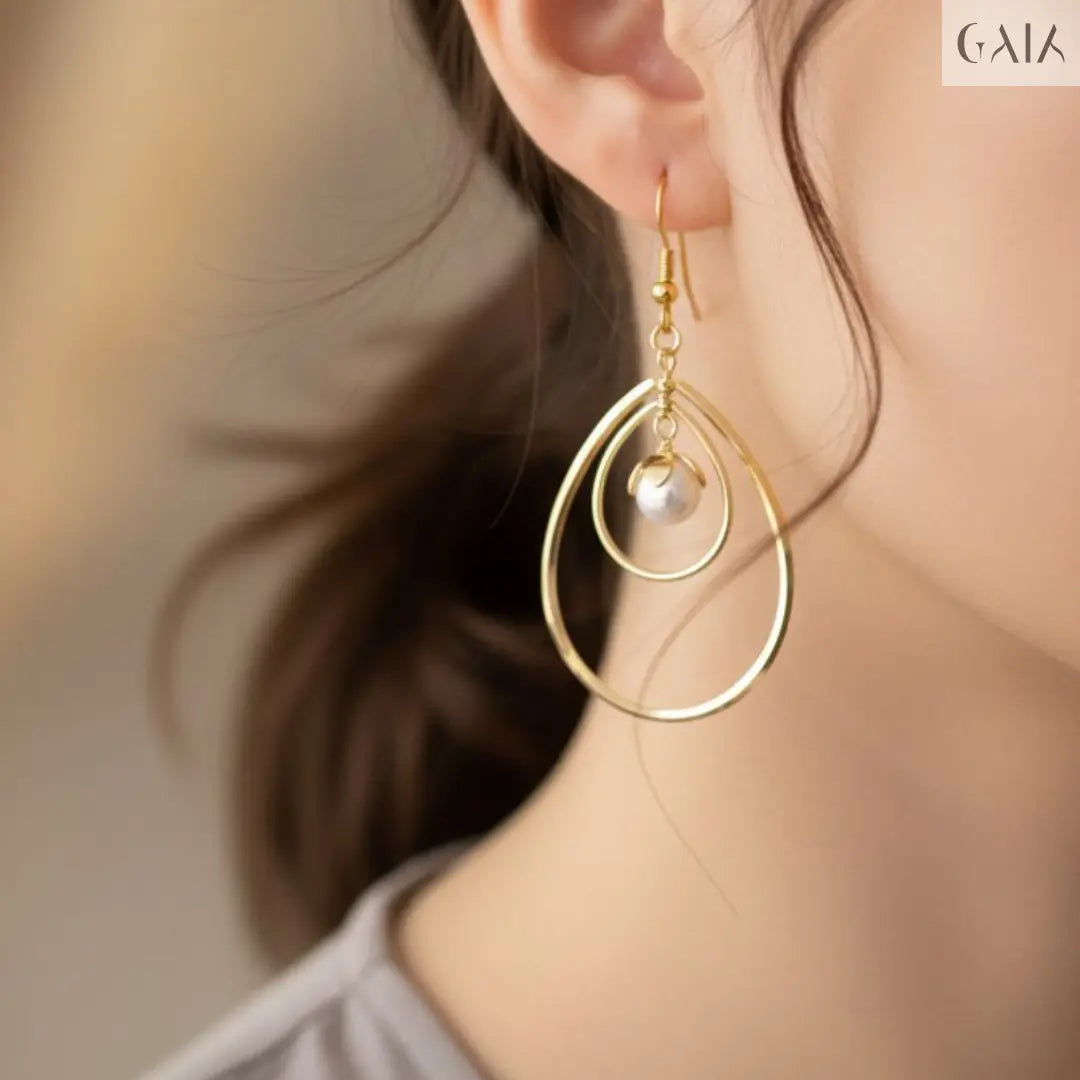 Close-up of a gold earring with a pearl drop worn by a person.