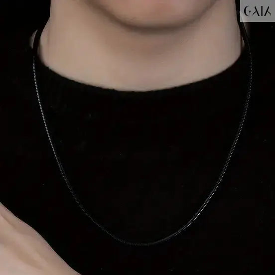 Person wearing a black necklace and bracelet against a dark background