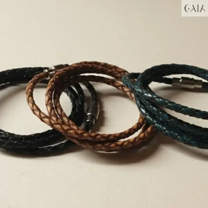 Three braided leather bracelets in black, brown, and blue on a beige background
