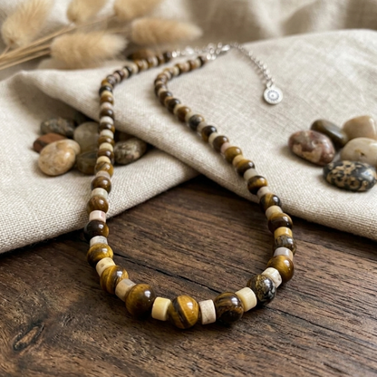 Necklace with brown and beige beads on a wooden surface with stones and fabric in the background