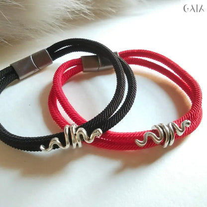 Two braided bracelets, one black and one red, with silver clasps on a fur background.