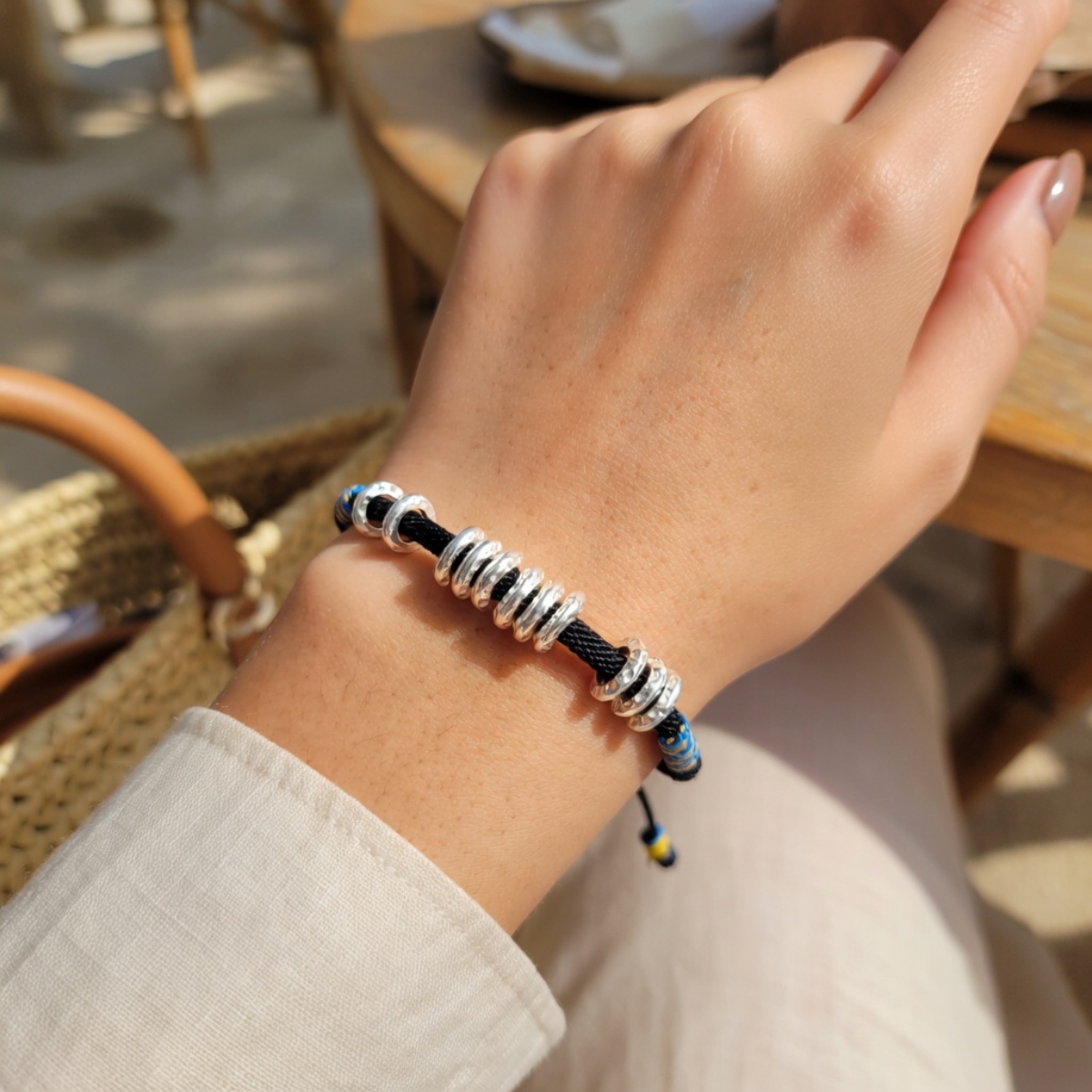 Woman wearing a black cord bracelet with silver beads and decorative accents.