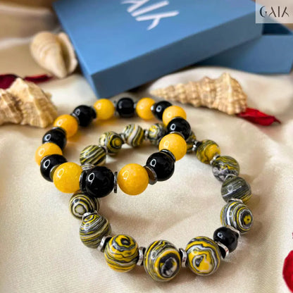 Set of beaded bracelets with yellow, black, and gray beads on a beige surface with a blue box in the background.