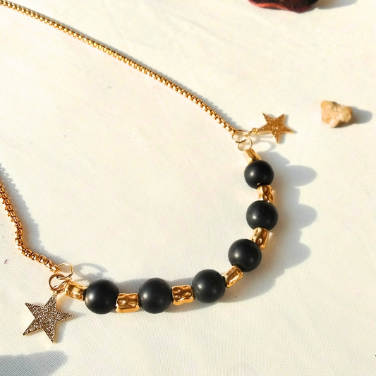 Bracelet with black beads and gold accents on a sandy background