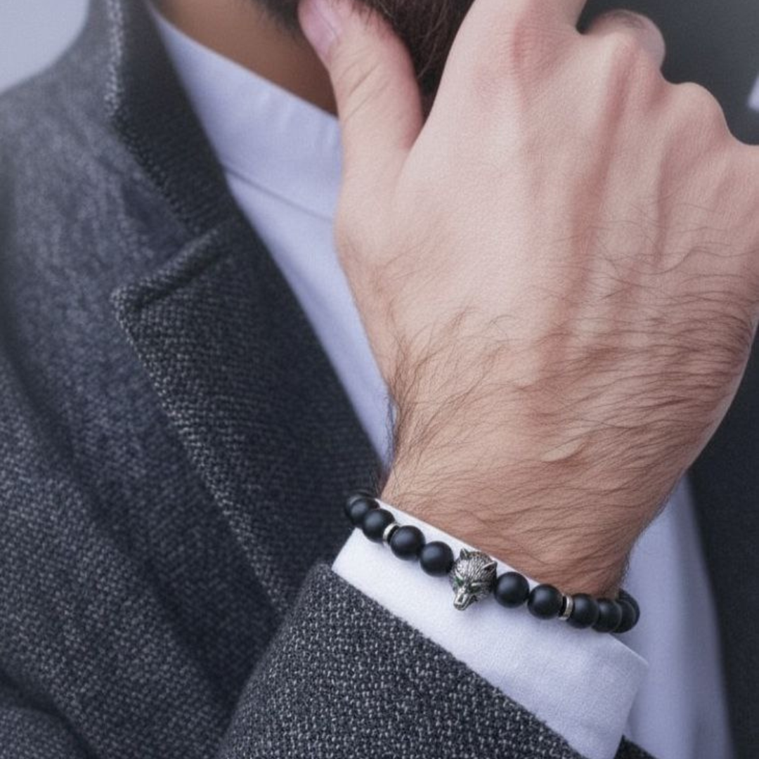 Person wearing a black beaded bracelet with a silver charm on a gray background